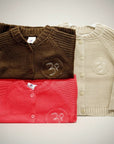 Stork And Baby infants cardigans in brown, red, and beige. Soft knit, button front, and embroidered logo detail.