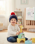 Stork And Baby navy and multi-tone knit winter hat with red pom-pom on a smiling baby