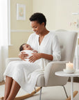 Stork And Baby Mothers Choice white acrylic baby shawl draped over a mother holding her newborn in a nursery chair.