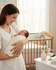 Stork And Baby Mothers Choice cream knitted shawl wrapping a sleeping newborn held by a smiling mother in a nursery.