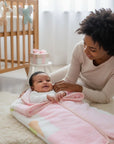 Stork And Baby Mothers Choice infant baby sac in soft pink and white, keeping a smiling baby cozy in a nursery setting.