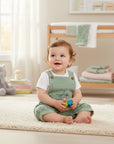 Stork And Baby light green muslin dungaree set with dinosaur print for baby boy, featuring wooden buttons and a white t-shirt.