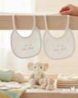 Stork And Baby white cotton bibs with blue trim and "Little Angel" embroidery, perfect for newborns.