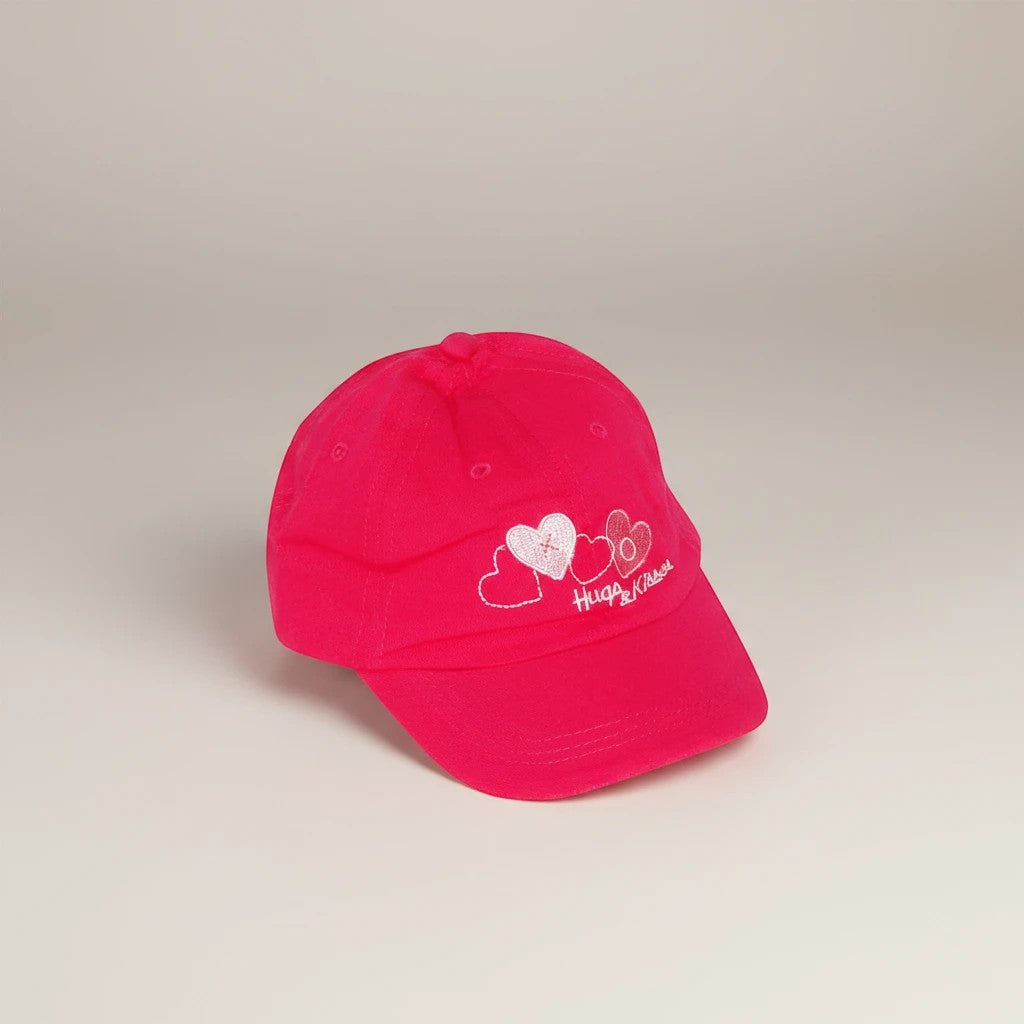 Stork And Baby pink cotton cap with embroidered hearts and "Hugs & Kisses" text for girls.