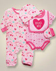 Stork And Baby pink 4-piece baby girl's outfit set with footie pajamas, bodysuit, bib, and hat featuring heart and candy prints.