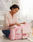 Stork And Baby Pink Nappy Bag Love with organized compartments and bottle holder. A woman is packing it in a nursery.