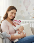 Stork And Baby pink striped knit infant hat with unicorn detail, worn by a sleeping baby held by a smiling mother.