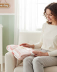 Stork & Baby pink and white infants cutwork blanket with house pattern, folded and held by a woman sitting in a chair.