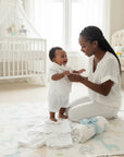 Stork And Baby white short-sleeve christening suit worn by a smiling baby boy with his mother in a nursery.