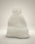 Stork And Baby white knit infant earflap hat with pom-pom, perfect for winter.