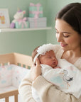 Stork And Baby white lace flower alice band with pearl detail worn by a newborn baby held by a mother in a nursery.