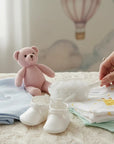 Stork And Baby white lace flower alice band with rose detail, held by hand on a nursery bed with baby accessories.