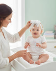Stork And Baby white satin girls alice band with bow and rose detail on a smiling baby held by her mother