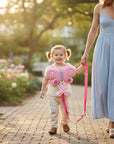 Stork And Baby pink butterfly harness with leash for toddlers, worn by a child walking with a woman in a garden.